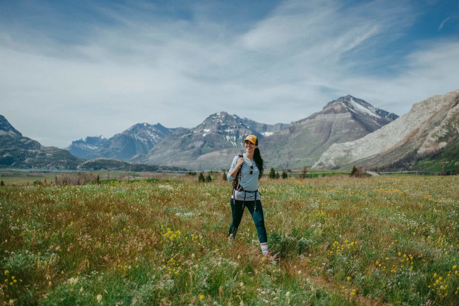 A visitor walks through wildflowers and grasses in Waterton with mountains in the distance.