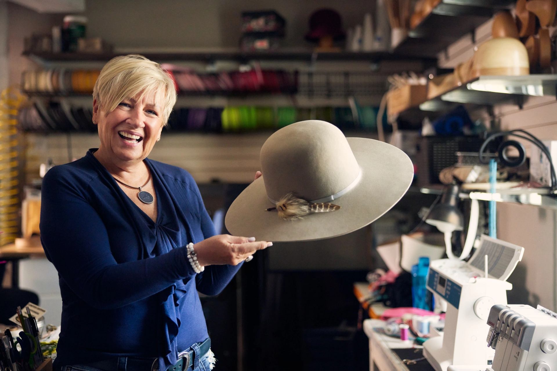 A smiling woman holds up a cowboy hat at Smithbilt Hats in Calgary.