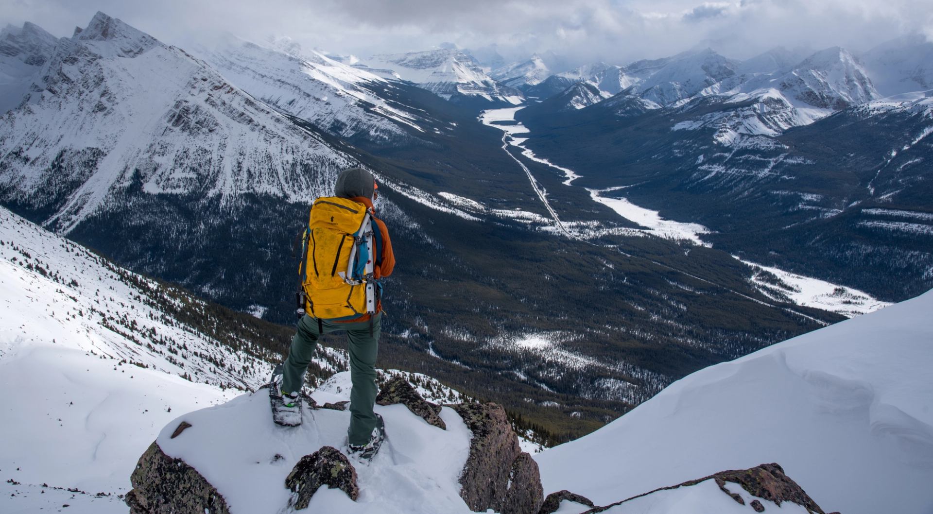 A person wearing snowshoes standing on a rock over looking the mountain view and valley below.