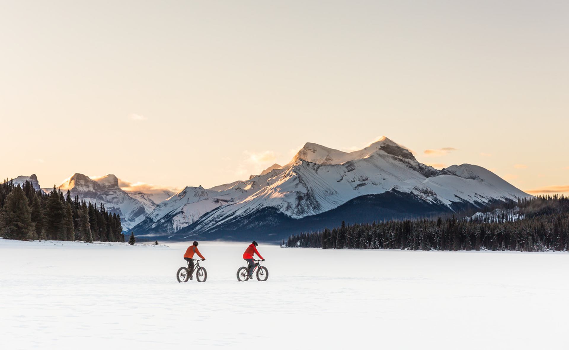 A wide angle shot of two people fatbiking on a frozen Maligne Lake at sunset in Jasper National Park