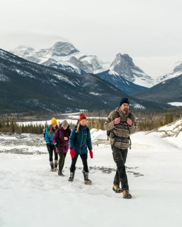 Group of people hiking on snow covered ground with mountains in the background.