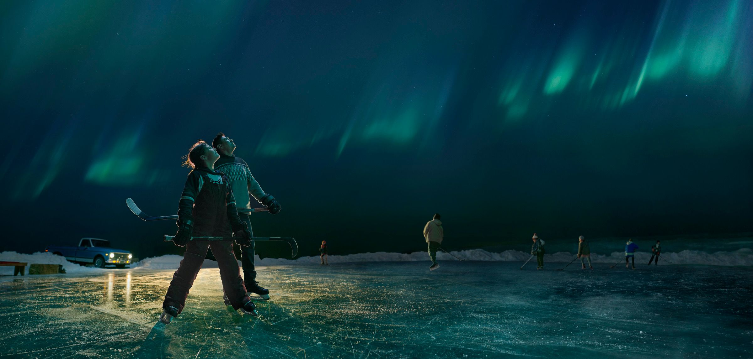 Hockey coach and player pausing from playing pond hockey to look up and admire the Northern Lights overhead