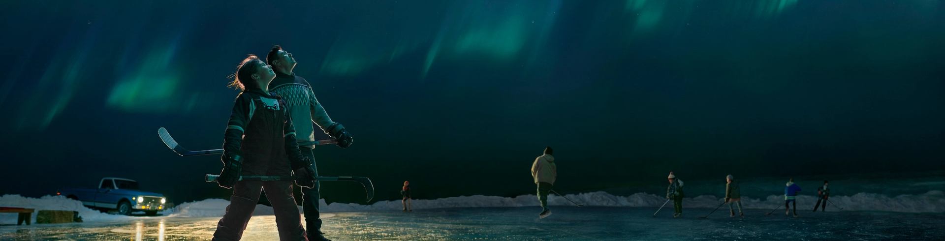 Hockey coach and player pausing from playing pond hockey to look up and admire the Northern Lights overhead
