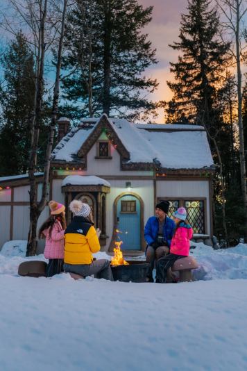Family sits in front of a fairytale cottage at Charmed Resorts