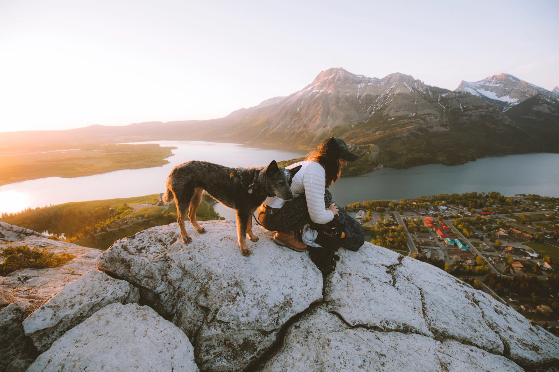 A woman and her dog pause on a trail overlooking the town of Waterton and its lakes.
