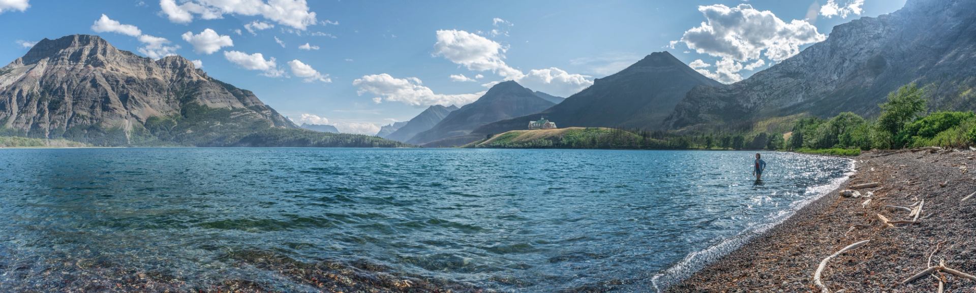 One person stands in the water close to shore with mountain views in Waterton National Park