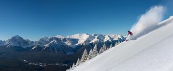 A skier rips down a slope at Lake Louise Ski Resort under a blue sky with the snow-capped Rockies in the background.