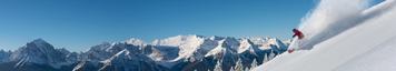 A person skiing down a mountain at Lake Louise Ski Resort, carving deep powder under blue skies.