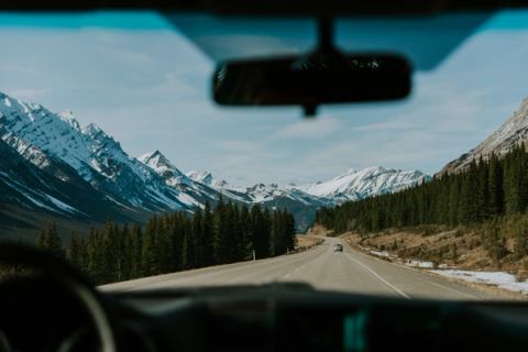 A dry winter highway in the Canadian Rockies is viewed through the front window of a vehicle.