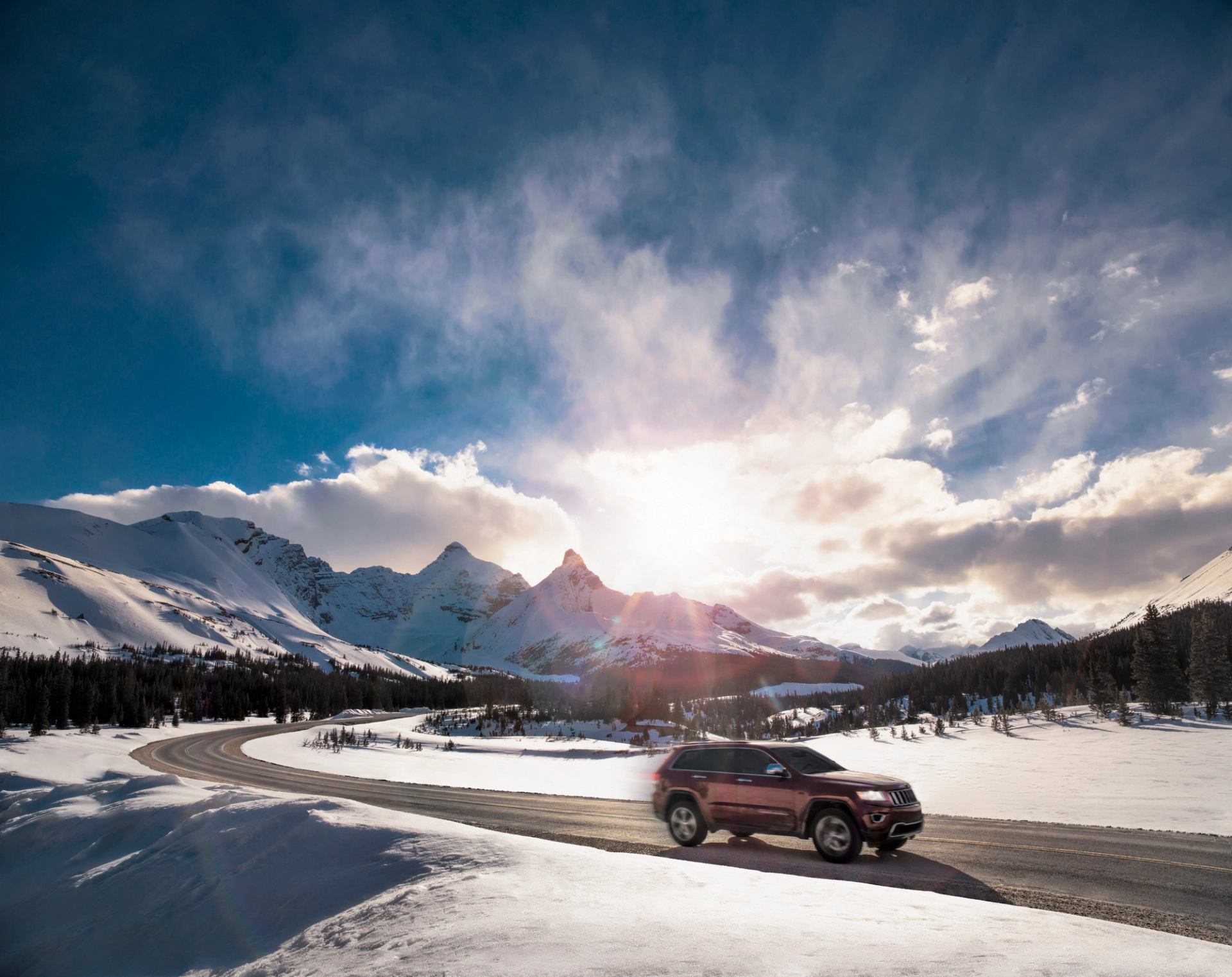 Vehicle driving on the Icefields Parkway highway with views of the mountains and sky.