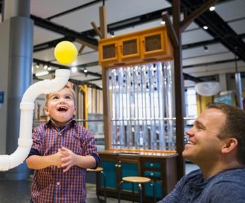 A father and son smiling while they play with a Science Centre interactive display.