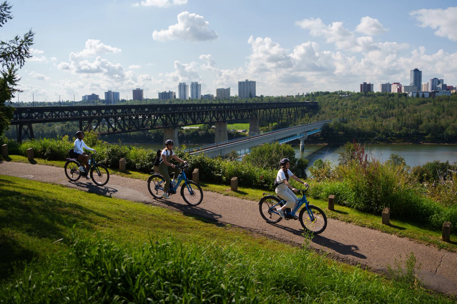 Cyclists bike a path overlooking Edmonton's green river valley, with bridges in the distance.