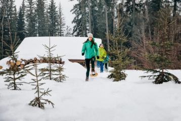 Friends snowshoeing away from a log cabin in the snowy forest.