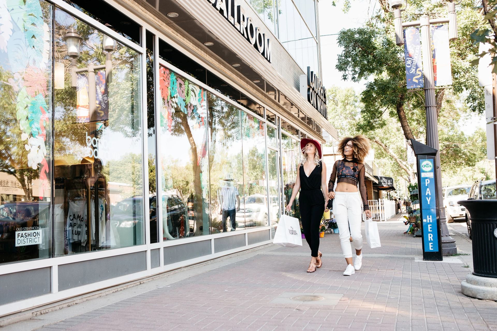 Two women carrying shopping bags look in a shop window as they walk down the street