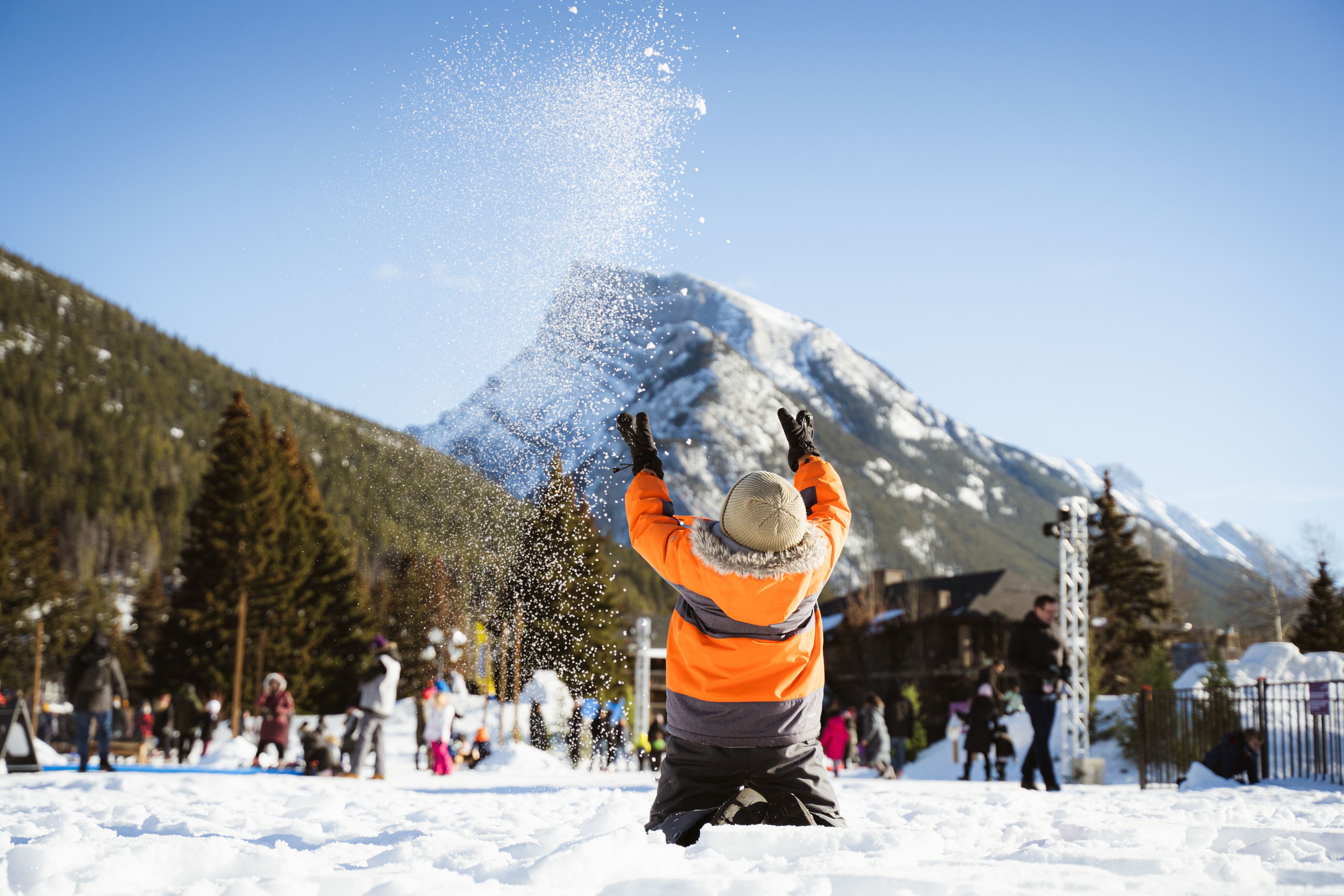 A child throwing snow up in the air with a mountain in the background.
