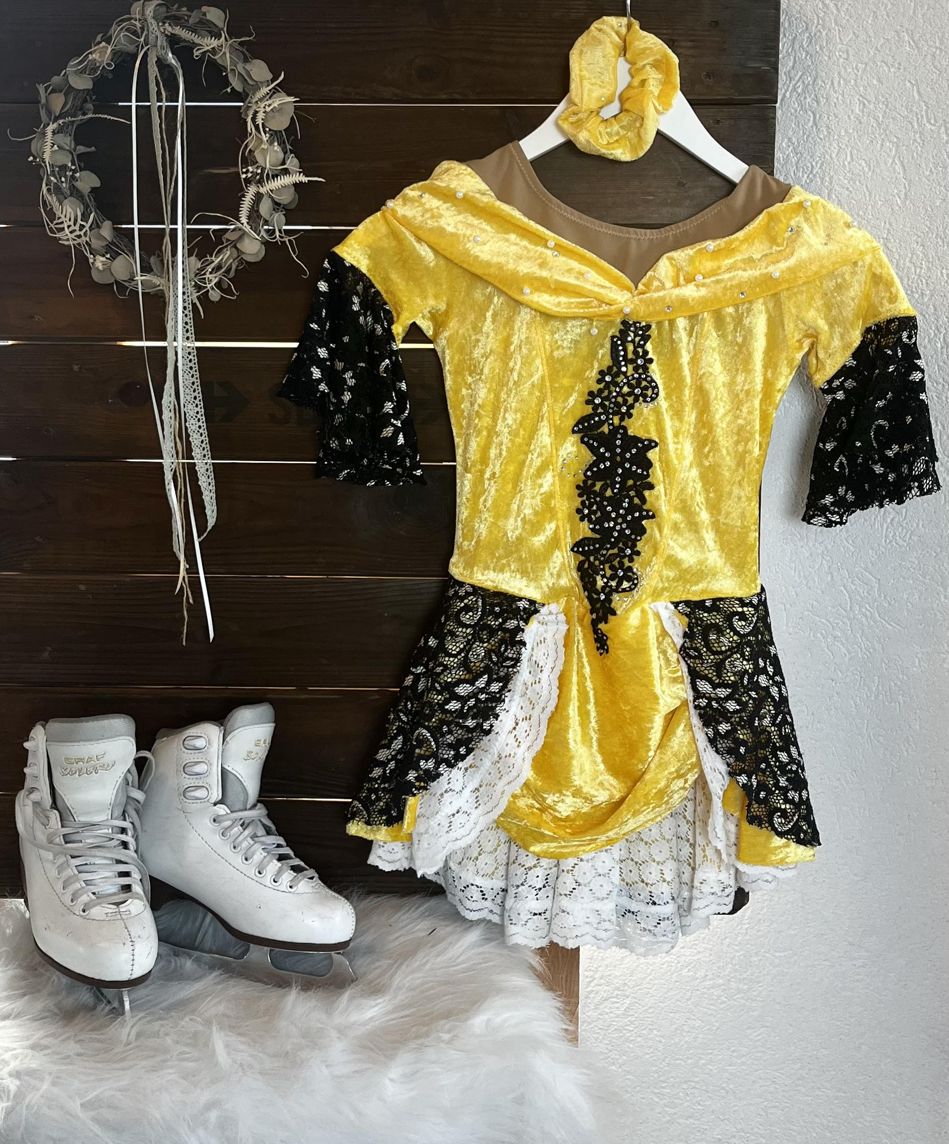 Gelb-schwarzes Kürkleid mit Spitze, daneben Schlittschuhe