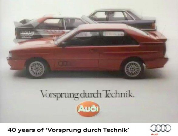 Advertisement featuring a stacked lineup of Audi Quattro models in red, each atop the other in decreasing size to create a visual illusion, with the slogan 'Vorsprung durch Technik' below, signifying 40 years of Audi's technological innovation.