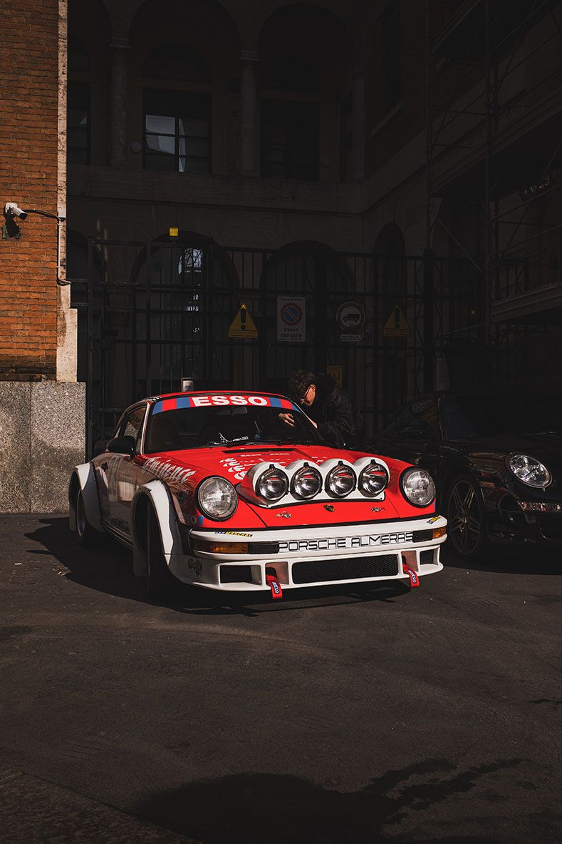Porsche da rally rossa e bianca parcheggiata in un’area in ombra, illuminata da un raggio di sole.