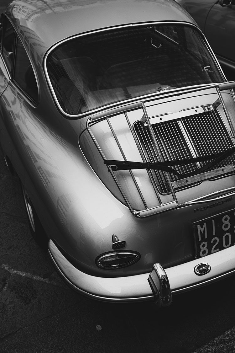 Vista posteriore in bianco e nero di una Porsche classica argento con griglia motore e portapacchi cromato.