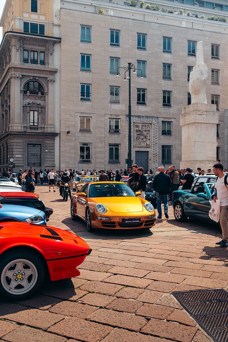 Ampia vista di Piazza Affari a Milano con numerose auto sportive e classiche esposte e persone tra le vetture.