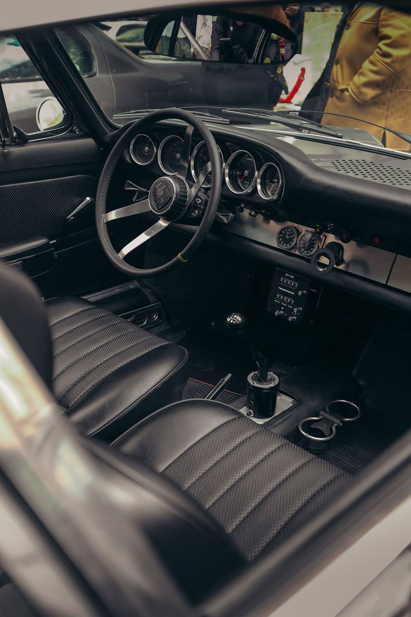 Interni neri di un’auto sportiva classica con volante sportivo, strumentazione analogica e cambio manuale.