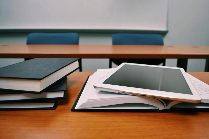 a desk with two chairs. several books are scattered on the table, and one is open with an ipad resting on top of it.