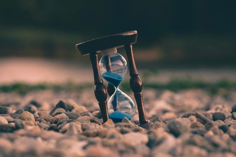 an hourglass sitting on a bed of rocks, coming close to the end