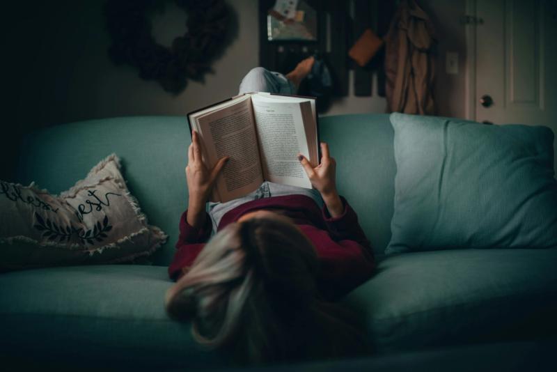 a woman sitting on a couch reading a book. top down view.
