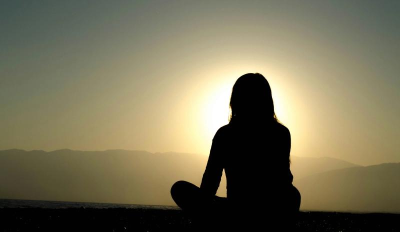 a girl sitting crosslegged in shadow and calmly looking out at the horizon