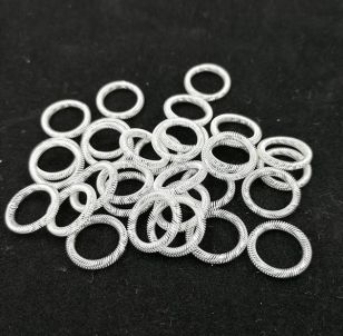 Loose silver-plated canted coil spring rings arranged in a pile on black background