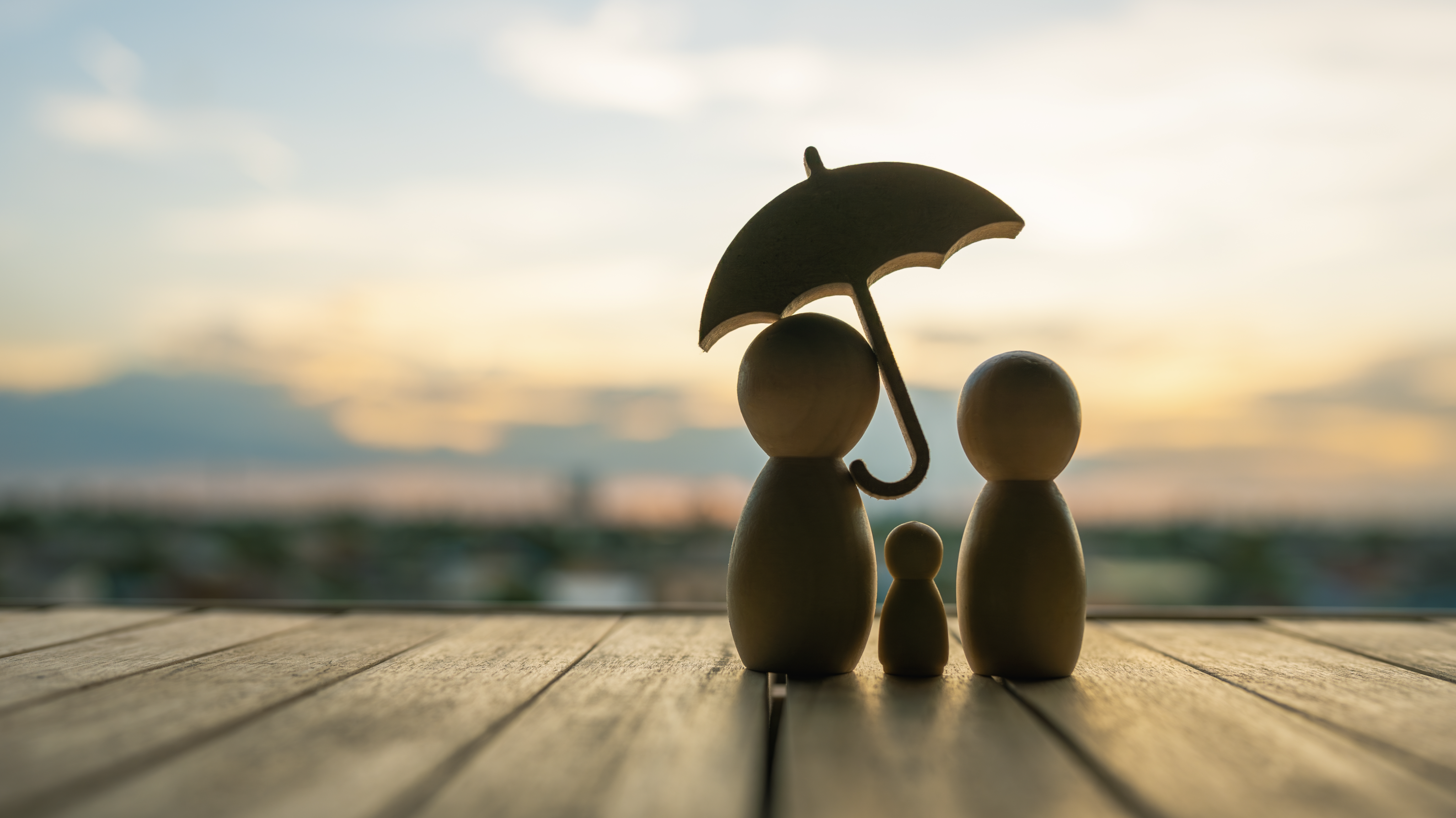 wooden figurines of a family standing under an umbrella
