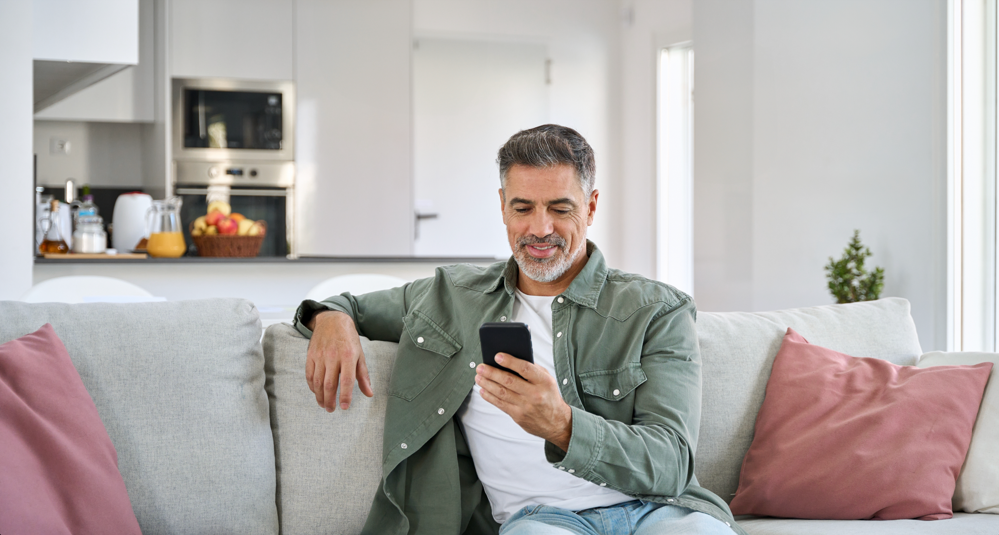 Man sat on couch at home, looking at his phone screen and smiling