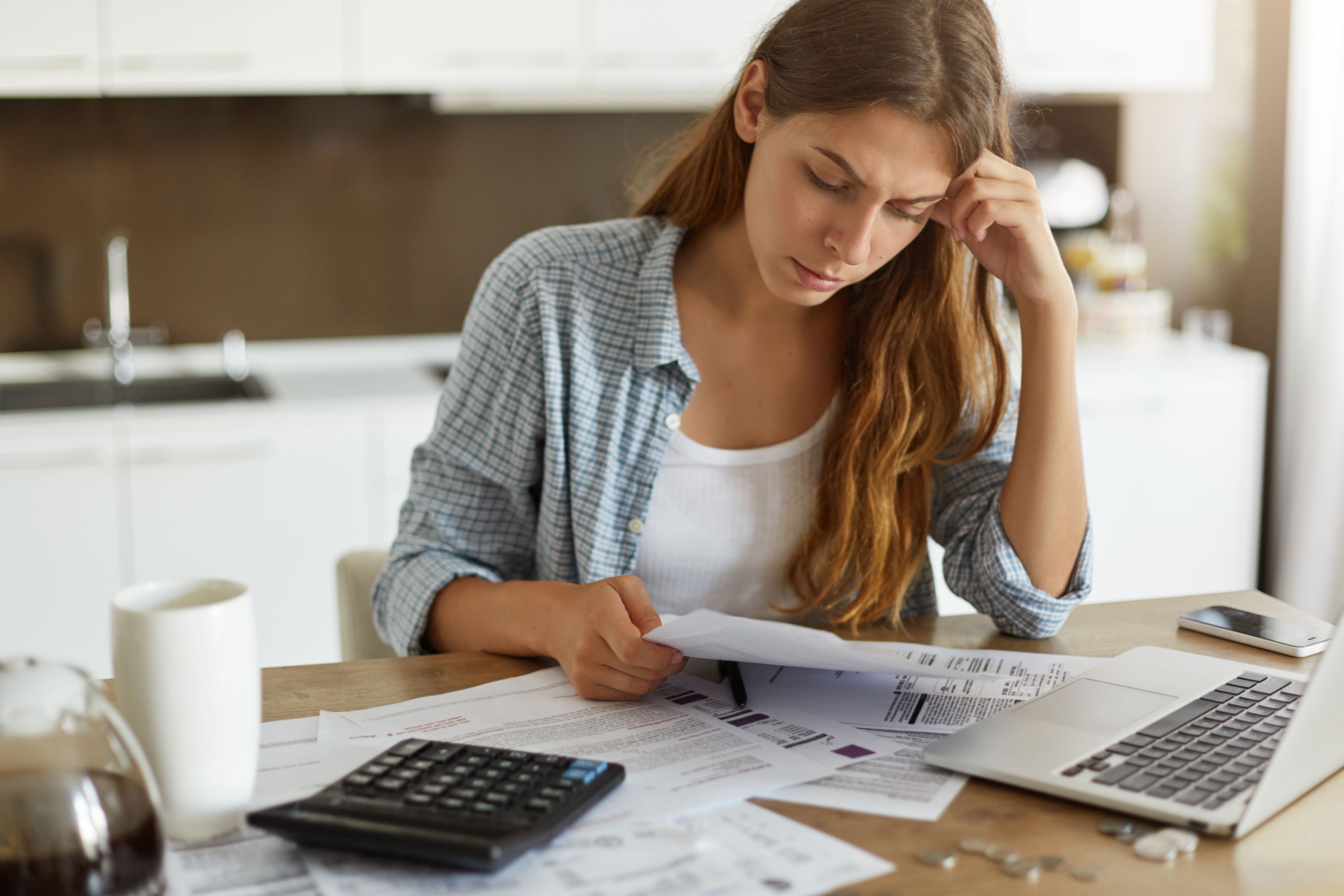 young woman looking very stressed as she reviews bills at her kitchen table