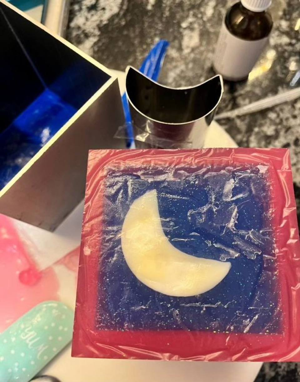 Jabón con una media luna crema sobre fondo azul y borde rosa