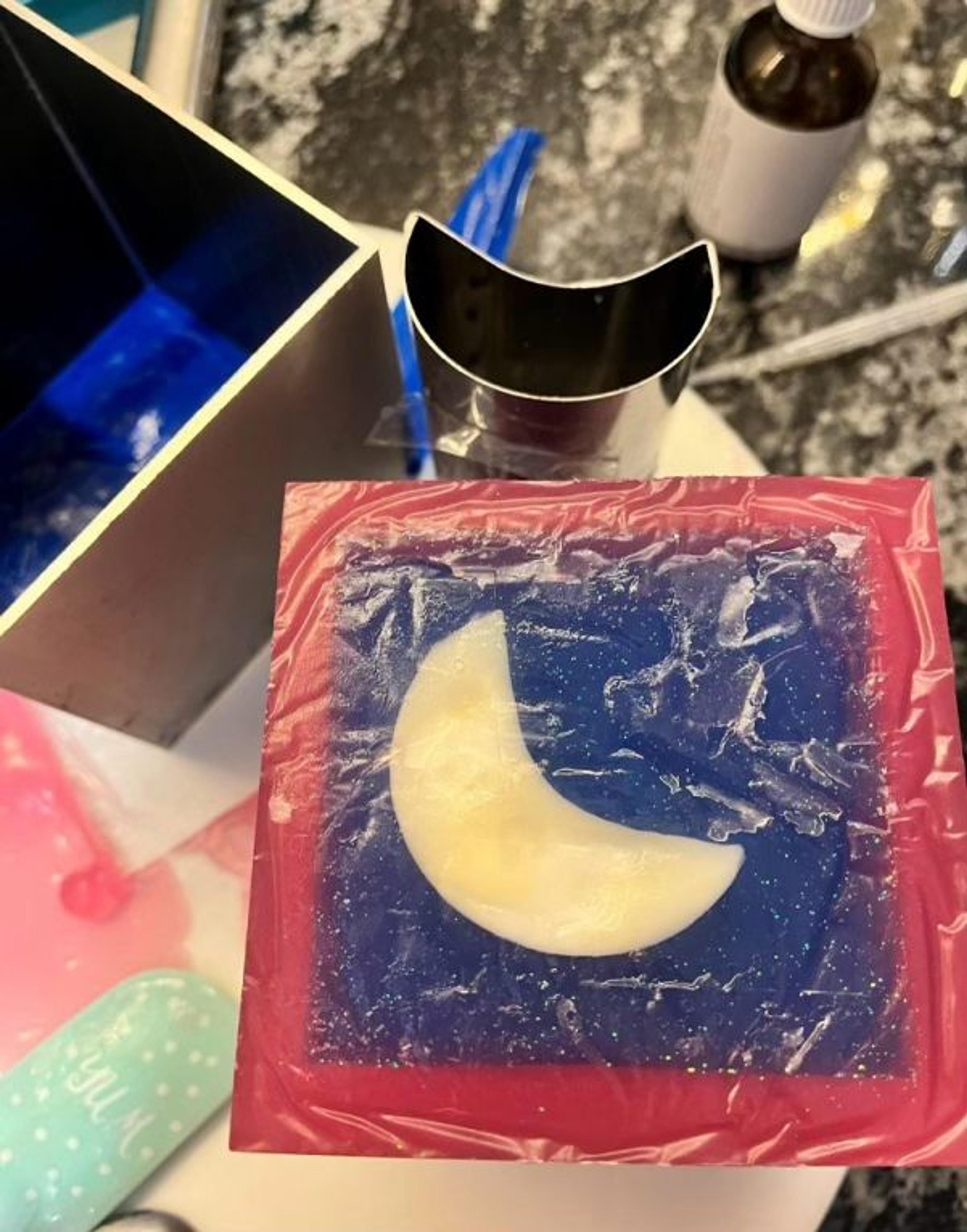 Jabón con una media luna crema sobre fondo azul y borde rosa