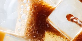 Close-up of espresso mixing with tonic over ice, showing bubbles and swirling brown liquid around large ice cubes