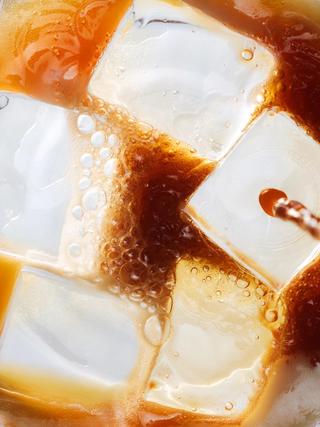 Close-up of espresso mixing with tonic over ice, showing bubbles and swirling brown liquid around large ice cubes