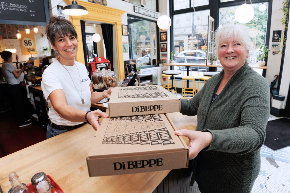 A women handing another women boxes of pizza inside a restaurant