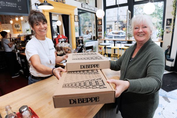 A women handing another women boxes of pizza inside a restaurant