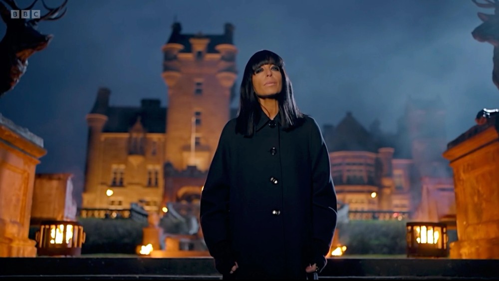 Host Claudia Winkleman in front of the lit castle in the reality series