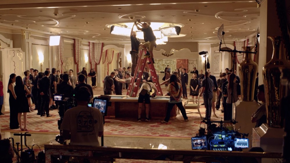 Crew work on location as extras and casino staff look on