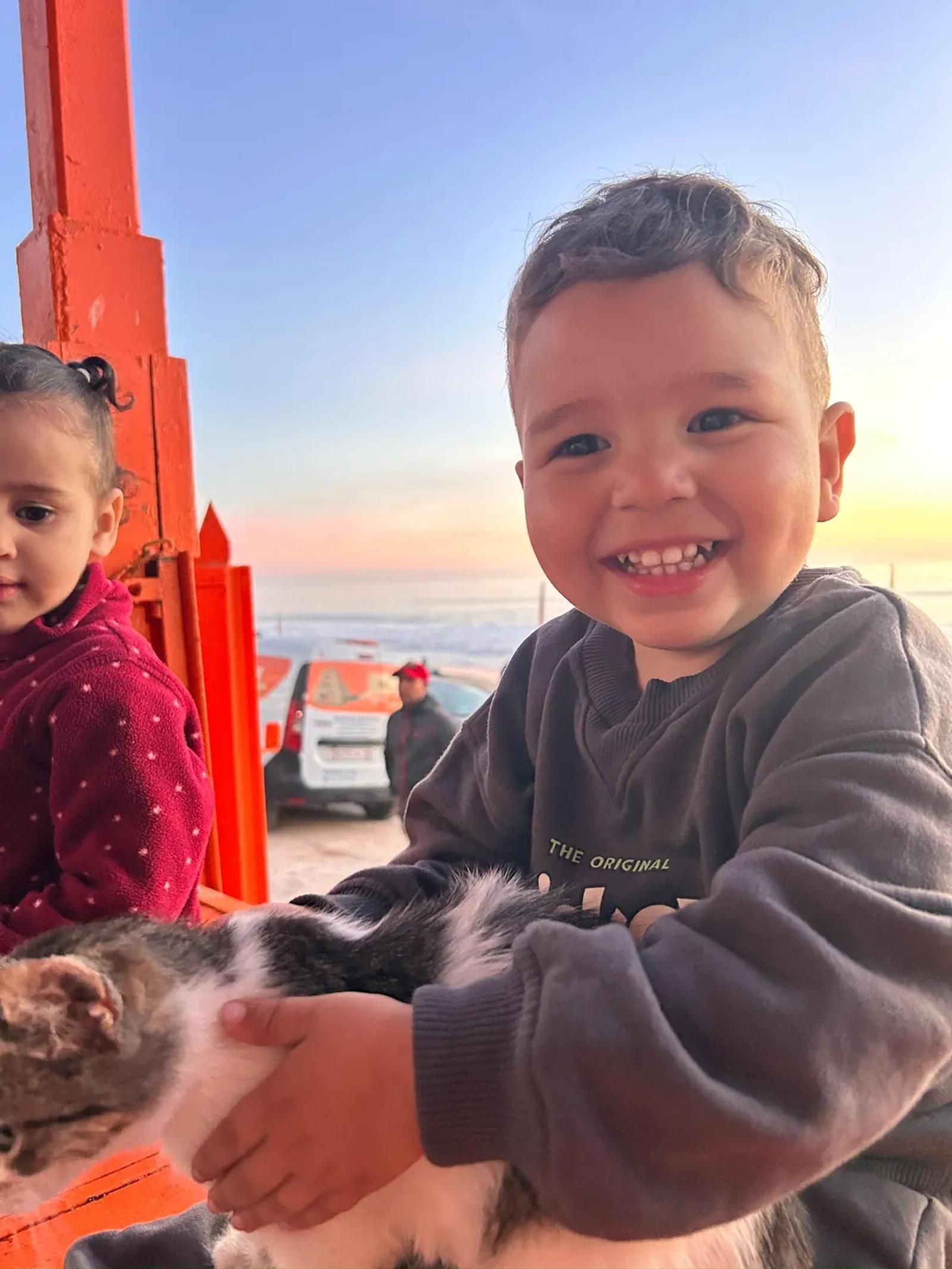 Un enfant sourit en tenant un chaton, au coucher du soleil