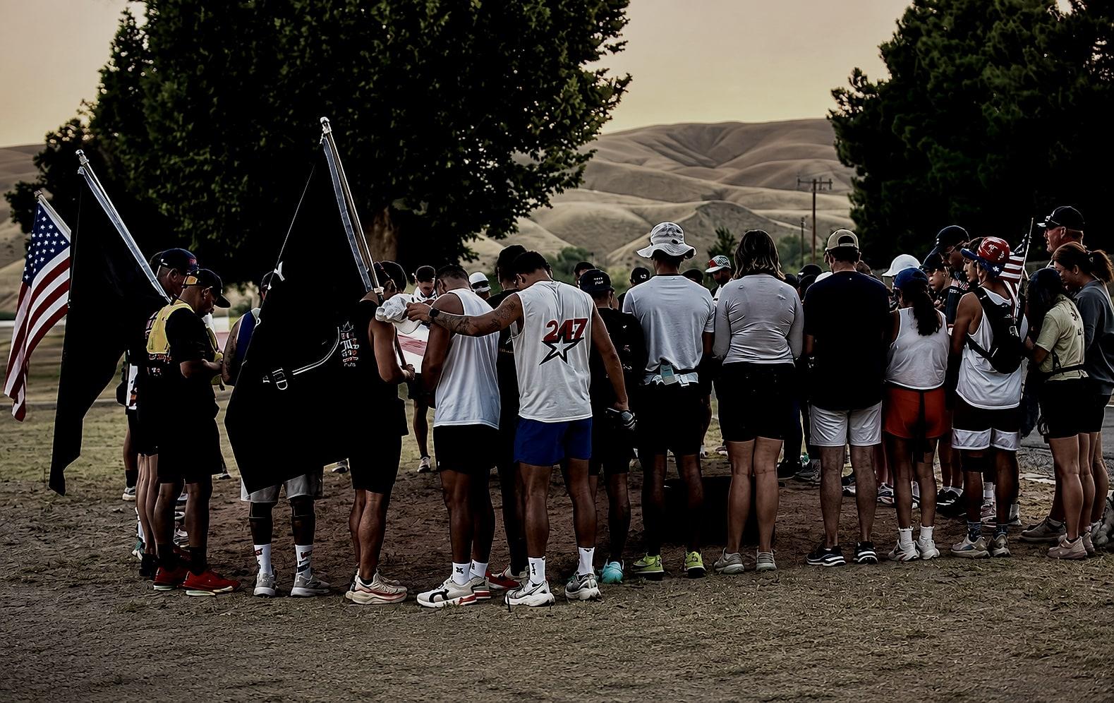 A team gathered in a tight huddle at sunset, arms around each other, flags raised behind them.