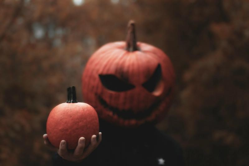 Person wearing scary jack o' lantern mask holding pumpkin