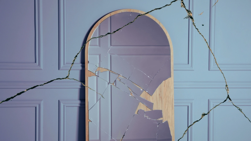 A cracked mirror set against blue wainscoting. Symbolizes repeated heresy.