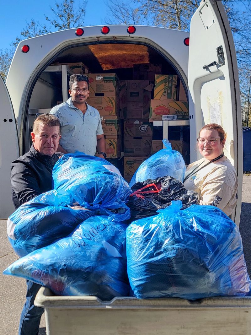 Three people loading a van with large blue bags of donated clothing