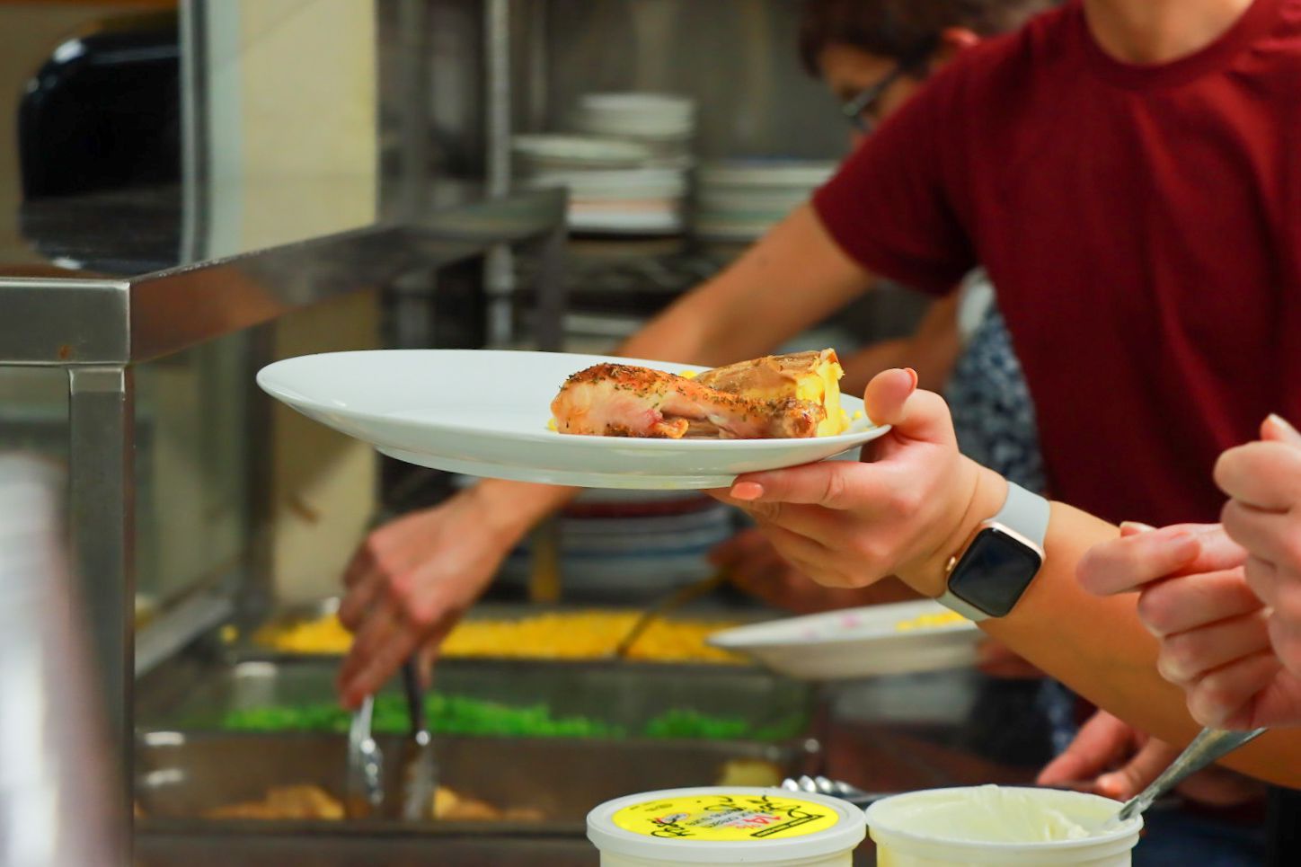 Person holding a plate with roasted chicken in a food serving line.