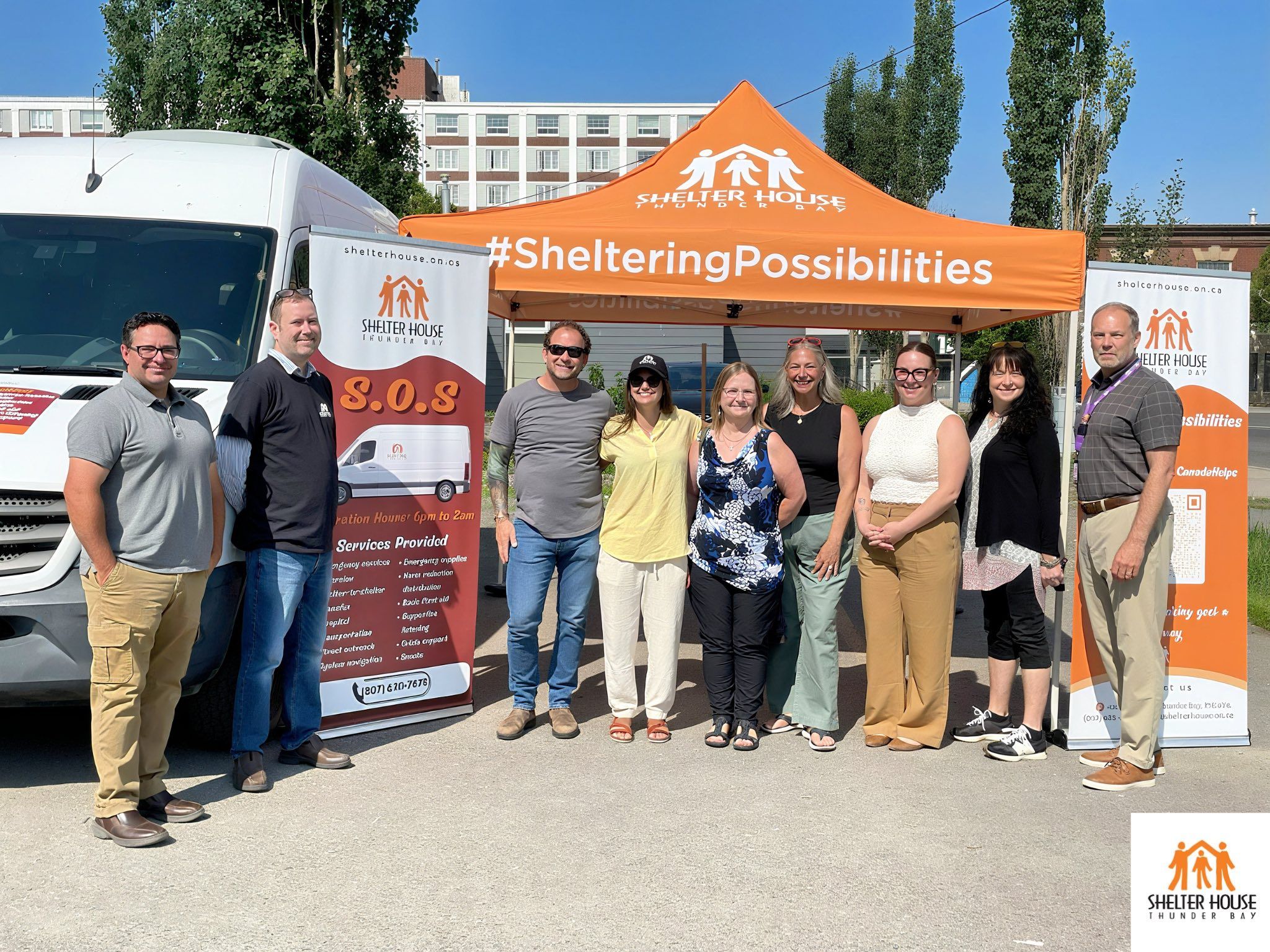 Shelter House Thunder Bay team members standing together outdoors under an orange Shelter House tent beside a service van.