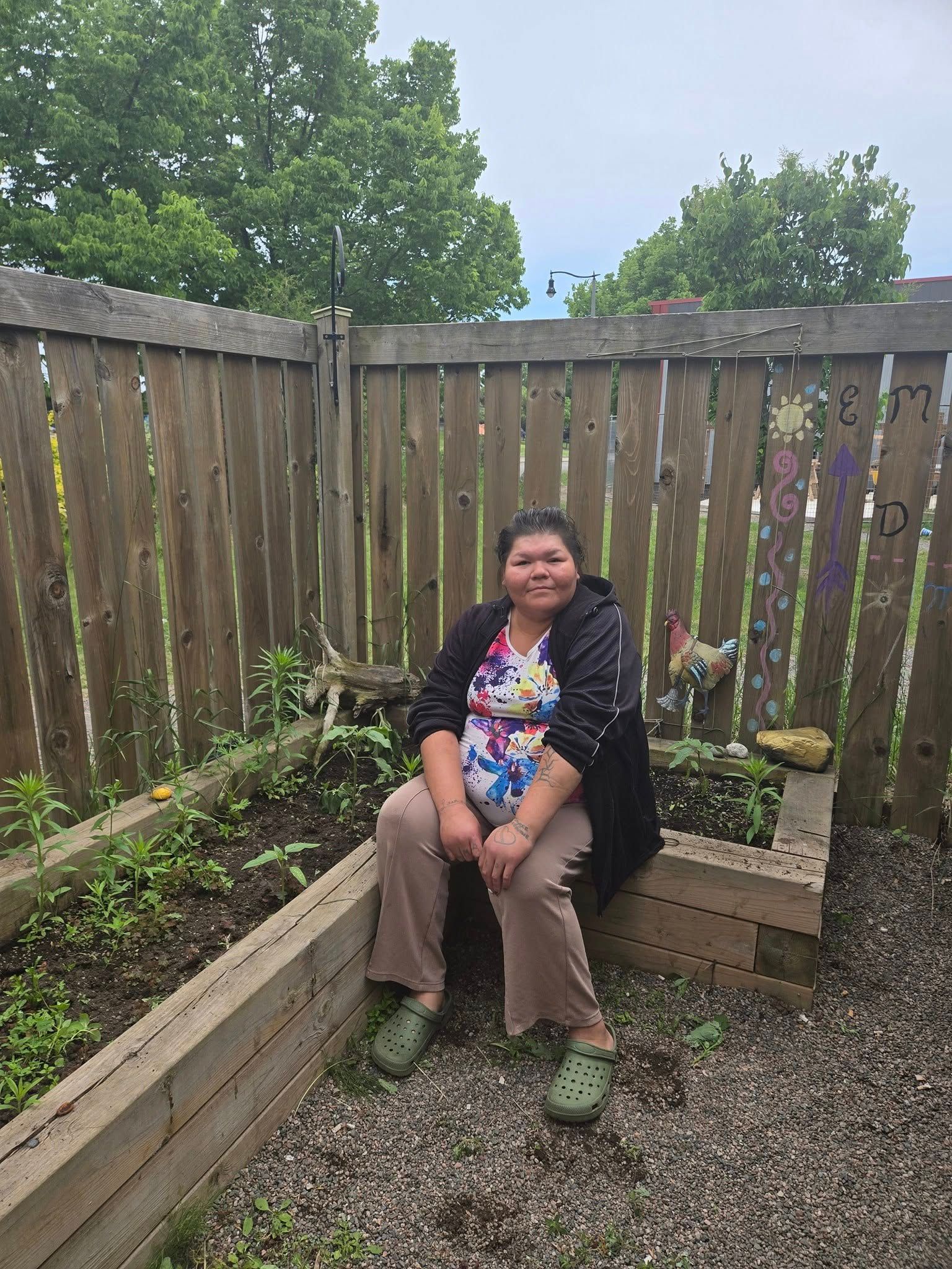 Person sitting in a small outdoor garden area with raised wooden garden beds.