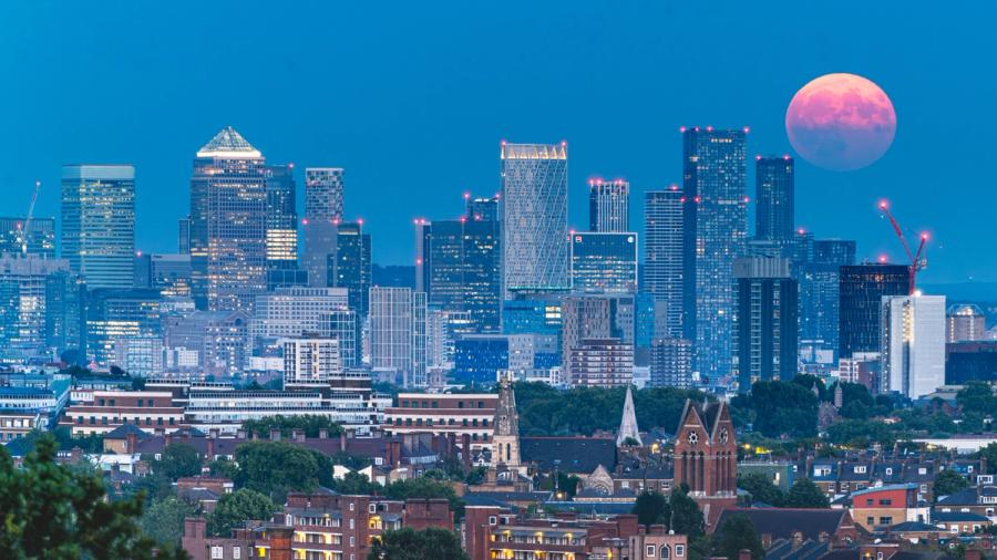 The full moon of July 2026 rises alongside the London skyline, showing the iconic Canary Wharf buildings.